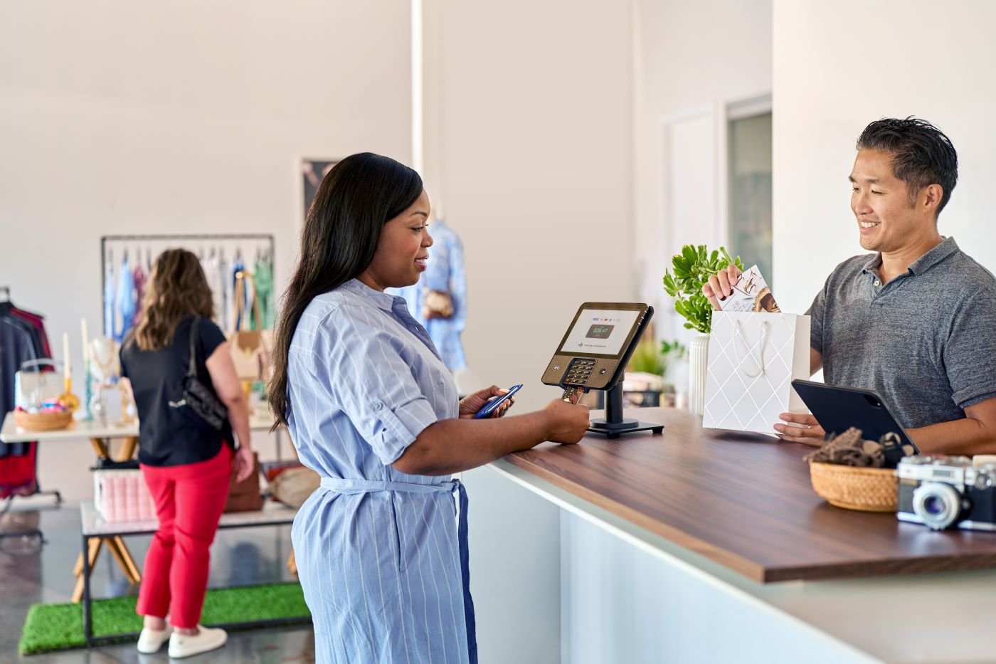 Woman making a payment with a card at a retail store counter while cashier places items in a shopping bag.